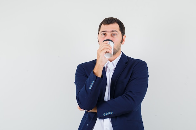 Young male in shirt and jacket drinking coffee and looking thoughtful