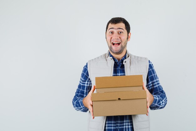 Young male in shirt,jacket holding boxes and looking glad , front view.