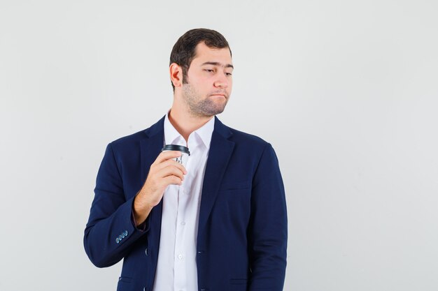 Young male in shirt, jacket holding cup of coffee and looking elegant