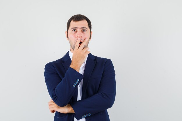 Young male in shirt and jacket holding hand on mouth and looking surprised