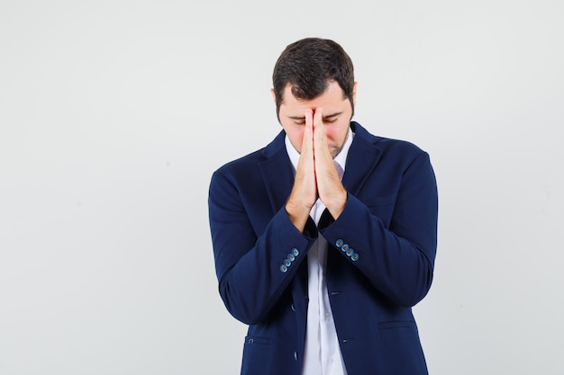 Young male in shirt and jacket holding hands in praying gesture and looking hopeful