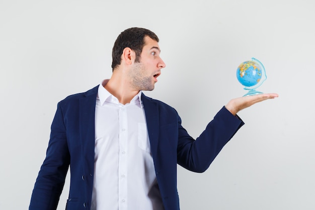 Foto gratuita giovane maschio in camicia e giacca guardando il globo della scuola e guardando stupito