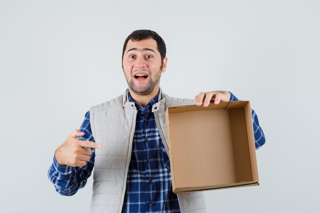 Молодой мужчина в рубашке, куртке, указывая на пустую коробку, вид спереди.