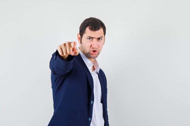 Young male in shirt, jacket pointing at front and looking nervous