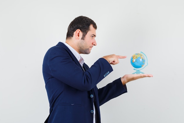 Young male in shirt and jacket pointing at school globe and looking focused .