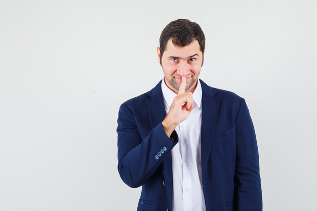 Young male in shirt and jacket showing silence gesture and looking confident