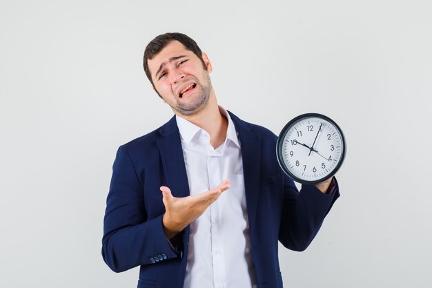 Young male in shirt and jacket showing wall clock and looking wistful