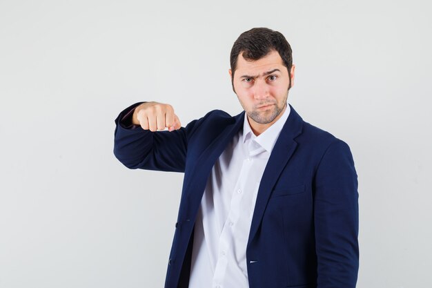 Young male in shirt, jacket threatening with fist and looking spiteful