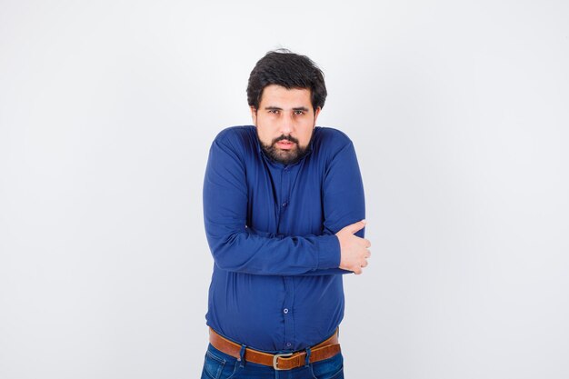 Young male in shirt, jeans hugging himself and looking sensible , front view.