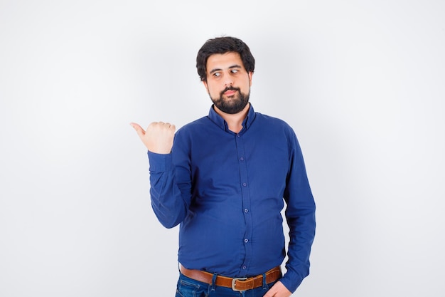 Young male in shirt, jeans showing middle thumb and looking confident , front view.