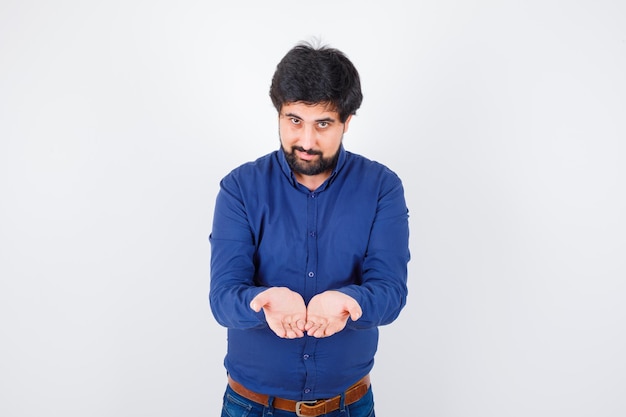 Young male in shirt, jeans stretching cupped hands and looking hopeful .