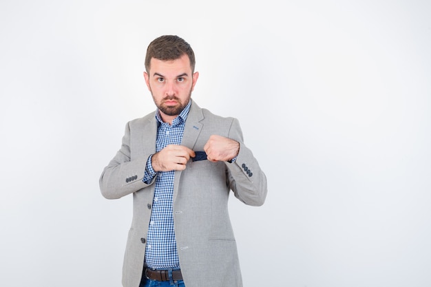 Young male in shirt, jeans, suit jacket keeping handkerchief of pocket and looking confident , front view.