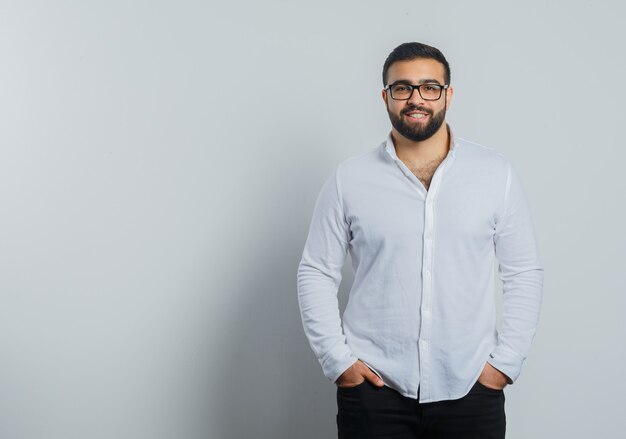 Young male in shirt, pants holding hands in pockets and looking confident