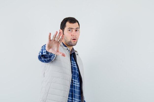 Молодой мужчина в рубашке, безрукавном пиджаке показывает жест остановки и выглядит сосредоточенным, вид спереди. место для текста