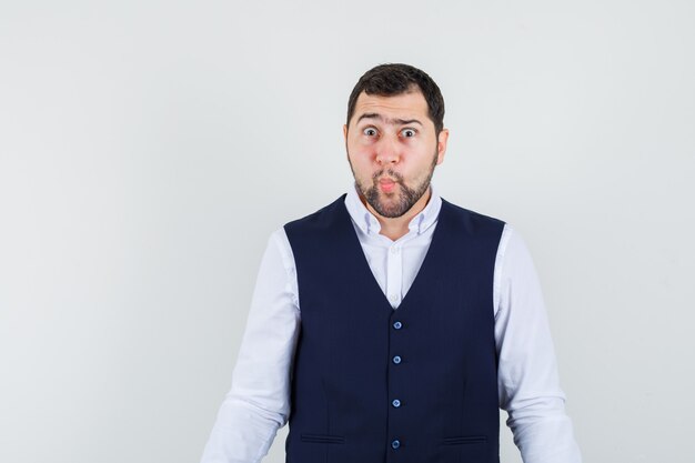 Young male in shirt, vest frowning eyebrows while looking at camera and looking puzzled