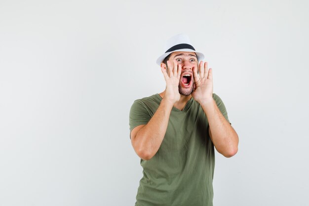 Young male shouting or announcing something in green t-shirt and hat front view.