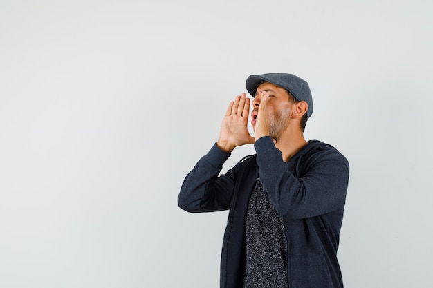 Young male shouting or announcing something in t-shirt, jacket, cap front view.