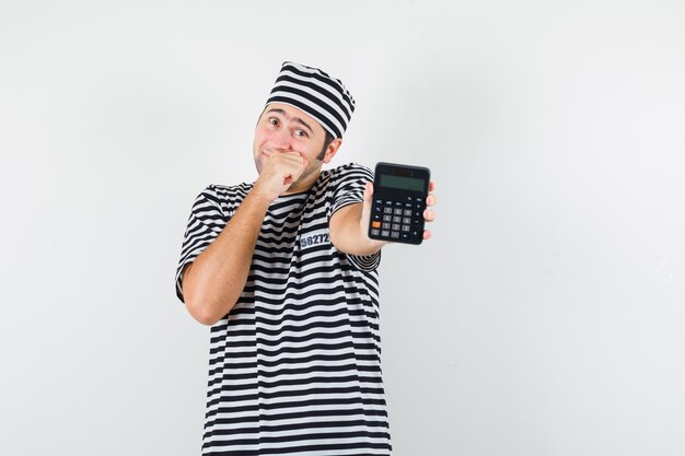 Giovane maschio che mostra calcolatrice in maglietta, cappello e che sembra vergognarsi. vista frontale.
