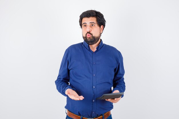 Young male showing calculator while discussing in royal blue shirt , front view.