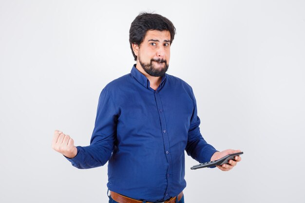 Young male showing calculator while showing winner gesture in royal blue shirt , front view.