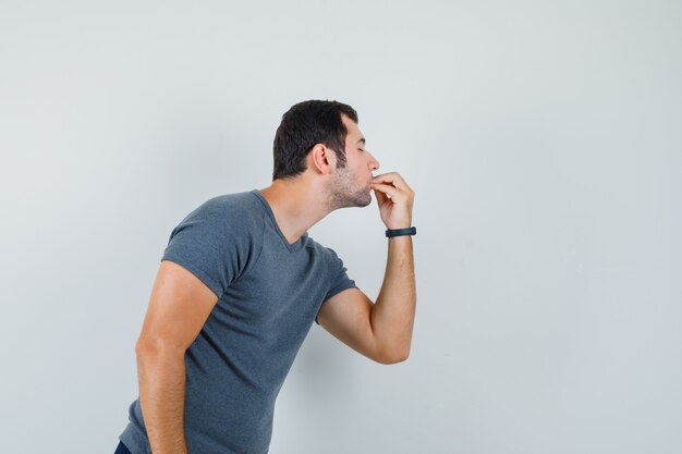 Young male showing delicious gesture in grey t-shirt and looking delighted 