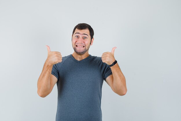 Young male showing double thumbs up in grey t-shirt and looking merry  