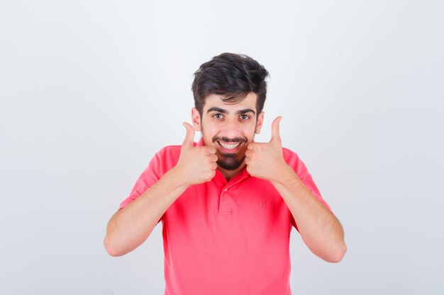 Young male showing double thumbs up in pink t-shirt and looking merry. front view.