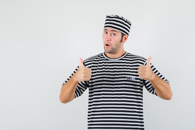 Free photo young male showing double thumbs up in t-shirt, hat and looking confident. front view.