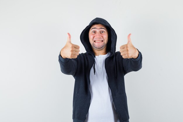 Young male showing double thumbs up in t-shirt, jacket and looking jolly. front view.