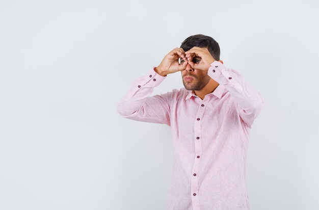 ピンクのシャツで眼鏡のジェスチャーを示し、焦点を当てて、正面図を見て若い男性。