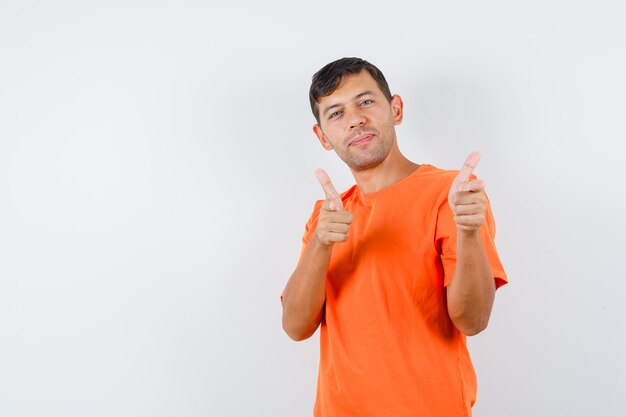Young male showing gun gesture pointed at camera in orange t-shirt and looking merry
