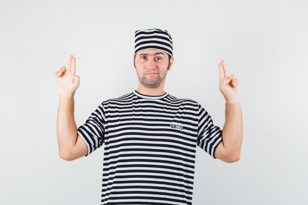 Young male showing gun gesture in t-shirt, hat and looking confident. front view.