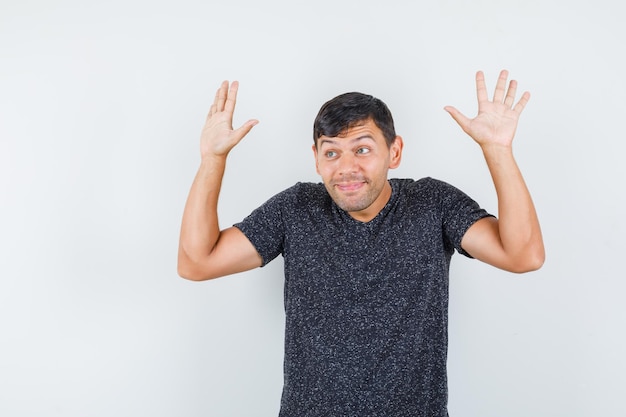 Young male showing helpless gesture in black t-shirt and looking confused , front view.