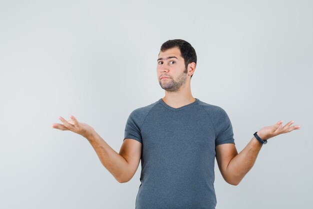 Young male showing helpless gesture in grey t-shirt and looking confused  