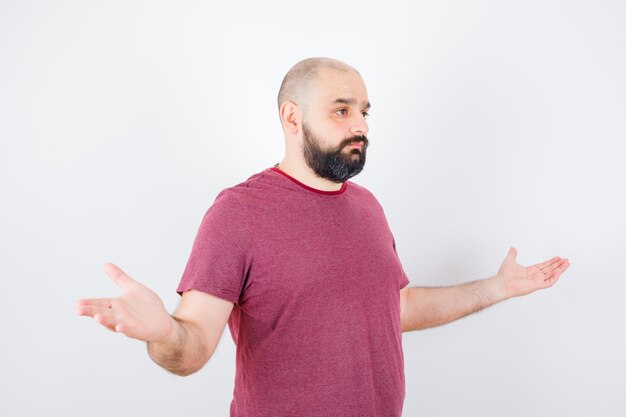 Young male showing helpless gesture in pink t-shirt and looking displeased .