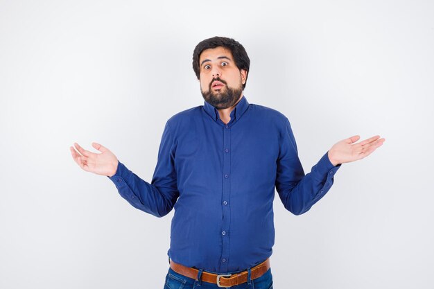 Young male showing helpless gesture in shirt, jeans and looking confused .