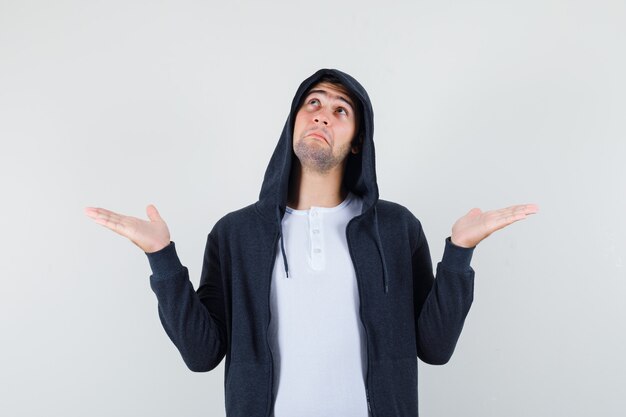 Young male showing helpless gesture in t-shirt, jacket and looking confused , front view.