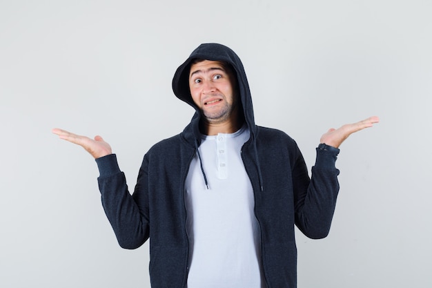 Young male showing helpless gesture in t-shirt, jacket and looking confused. front view.