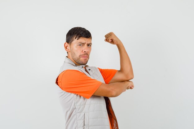 Young male showing his arm muscles in t-shirt, jacket and looking powerful. front view.