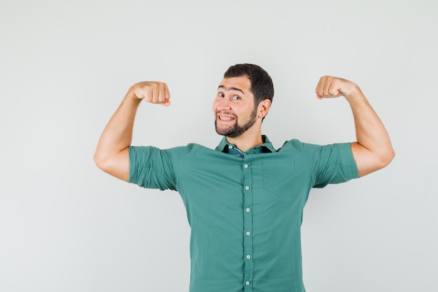 Foto gratuita giovane maschio che mostra i muscoli delle braccia in camicia verde e sembra energico, vista frontale.