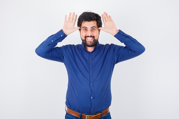 Young male showing horn gesture in royal blue shirt and looking funny , front view.