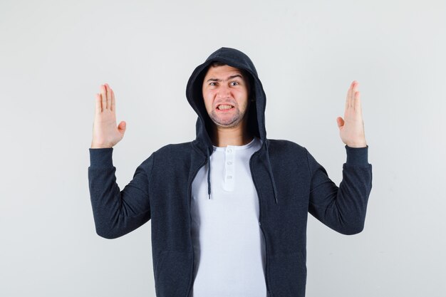 Молодой мужчина показывает жест отбивной каратэ в футболке, куртке и злобно смотрит, вид спереди.
