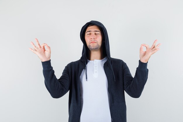 Молодой мужчина показывает жест медитации в футболке, куртке и выглядит расслабленным. передний план.