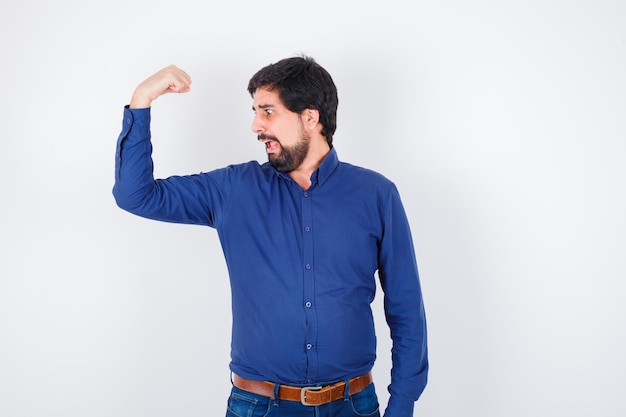 Free photo young male showing muscle of arm in shirt, jeans and looking amazed. .