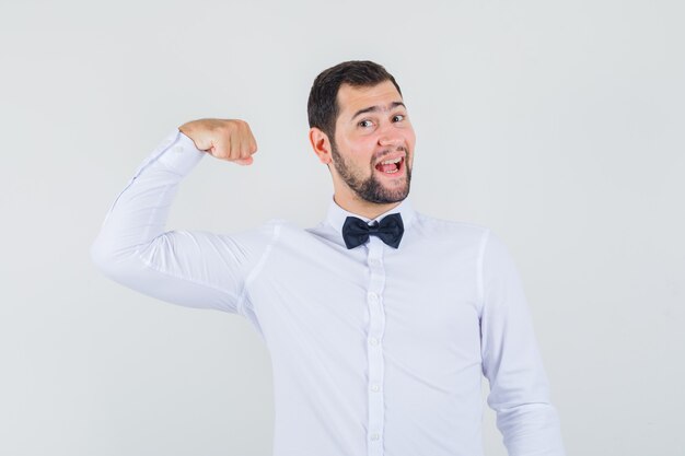 Young male showing muscles of arm in white shirt and looking happy. front view.