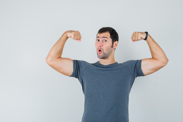 灰色のTシャツで腕の筋肉を示し、力強く見える若い男性