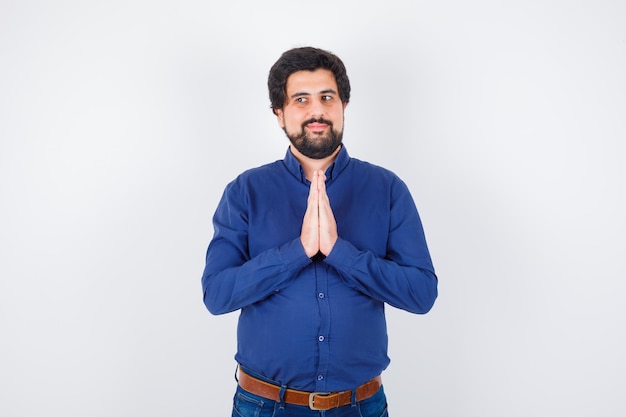 Young male showing namaste gesture in royal blue shirt front view.