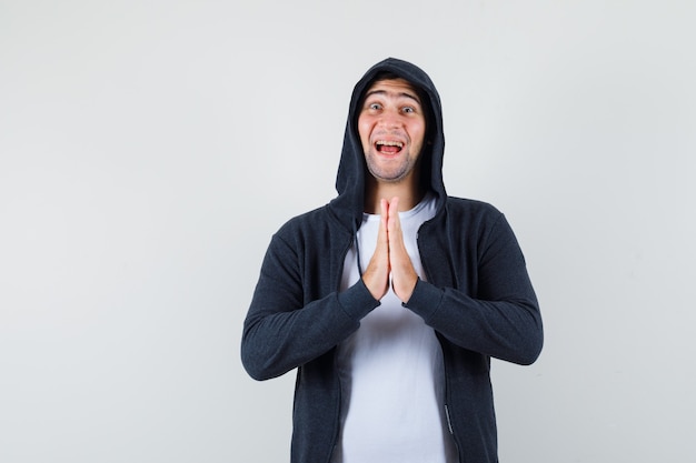 Young male showing namaste gesture in t-shirt, jacket and looking happy. front view.