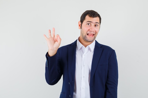 Young male showing ok gesture in shirt and jacket and looking confident