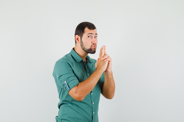 Young male showing pistol gesture in green shirt and looking careful. front view.